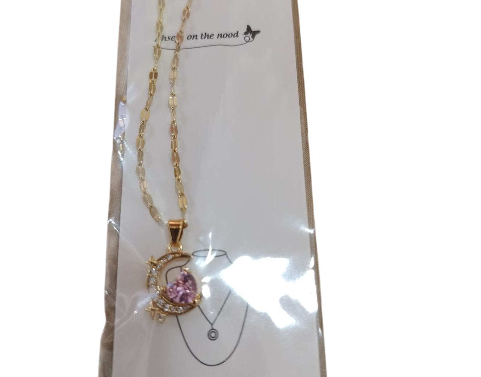 Collar de oro con colgante de piedra preciosa rosa en una tarjeta de presentación blanca.