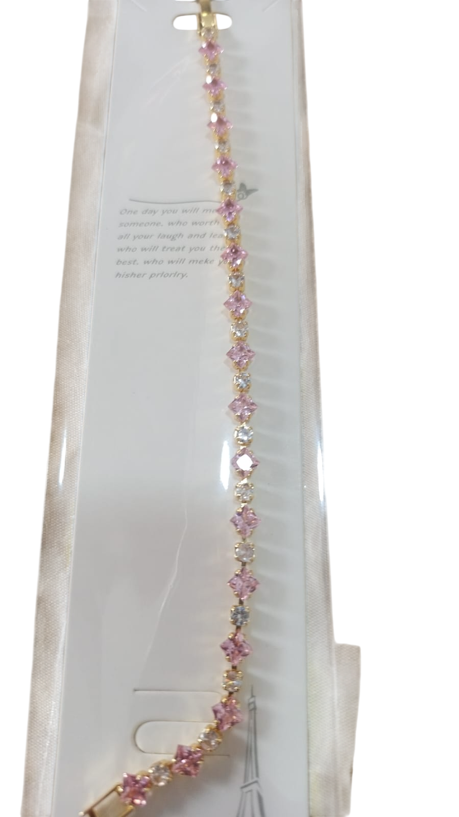 Collar de cuentas rosas y doradas colgando de un envase blanco con el texto de la etiqueta del producto.