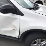 A white car with a dented passenger-side front door and a slightly misaligned fender panel.