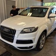 A person in a black shirt wipes the windshield of a clean white Audi SUV inside a garage.