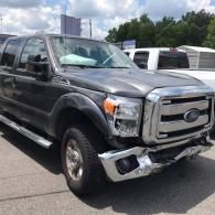 A gray Ford Super Duty pickup truck with a dented front bumper parked in an outdoor lot on a sunny day.
