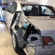 A silver Lexus in a repair shop with its rear bumper and quarter panel removed, revealing the inner body structure.