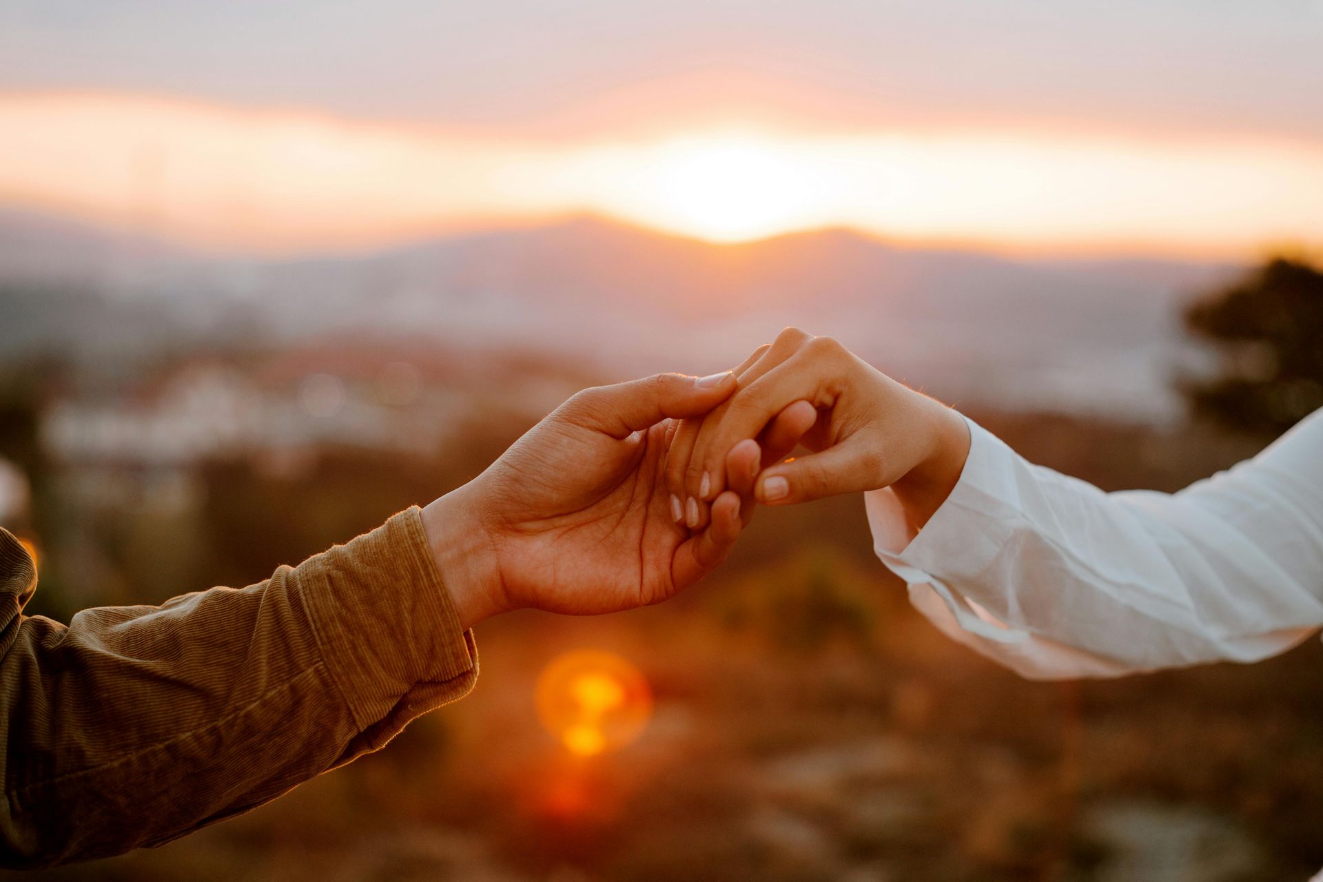 Two hands reaching for each other against a warm sunset backdrop; a gesture of connection.
