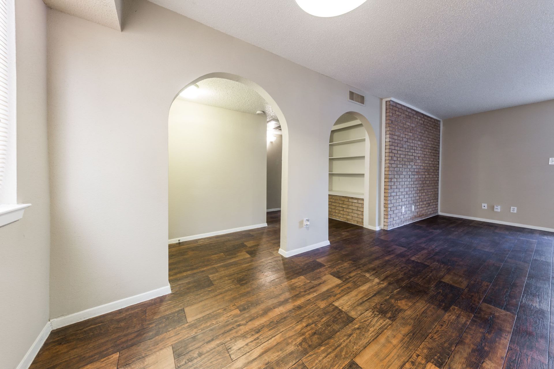 An empty living room with hardwood floors, a shelf, and a brick wall at SoCo on the Lake in Austin, TX.