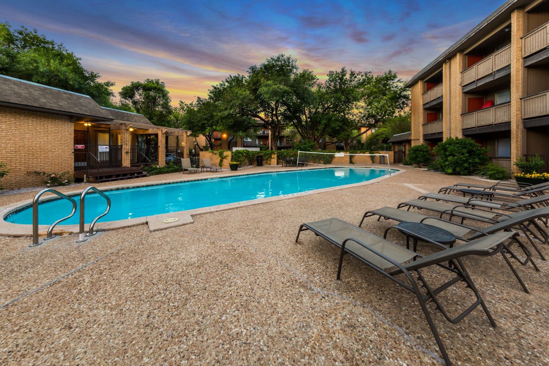 A large swimming pool surrounded by lounge chairs in front of apartment buildings at SoCo on the Lake in Austin, TX.
