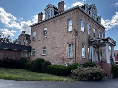 Brick office building with white-trimmed windows, manicured shrubs, and a front porch under a cloudy sky