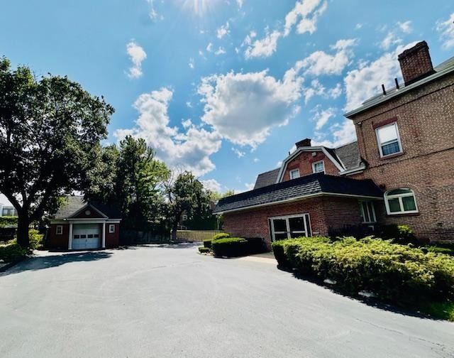 Brick building and small house beside an empty paved driveway under a bright blue sky with clouds