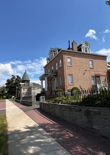 Brick house along a sunny sidewalk under a blue sky with clouds