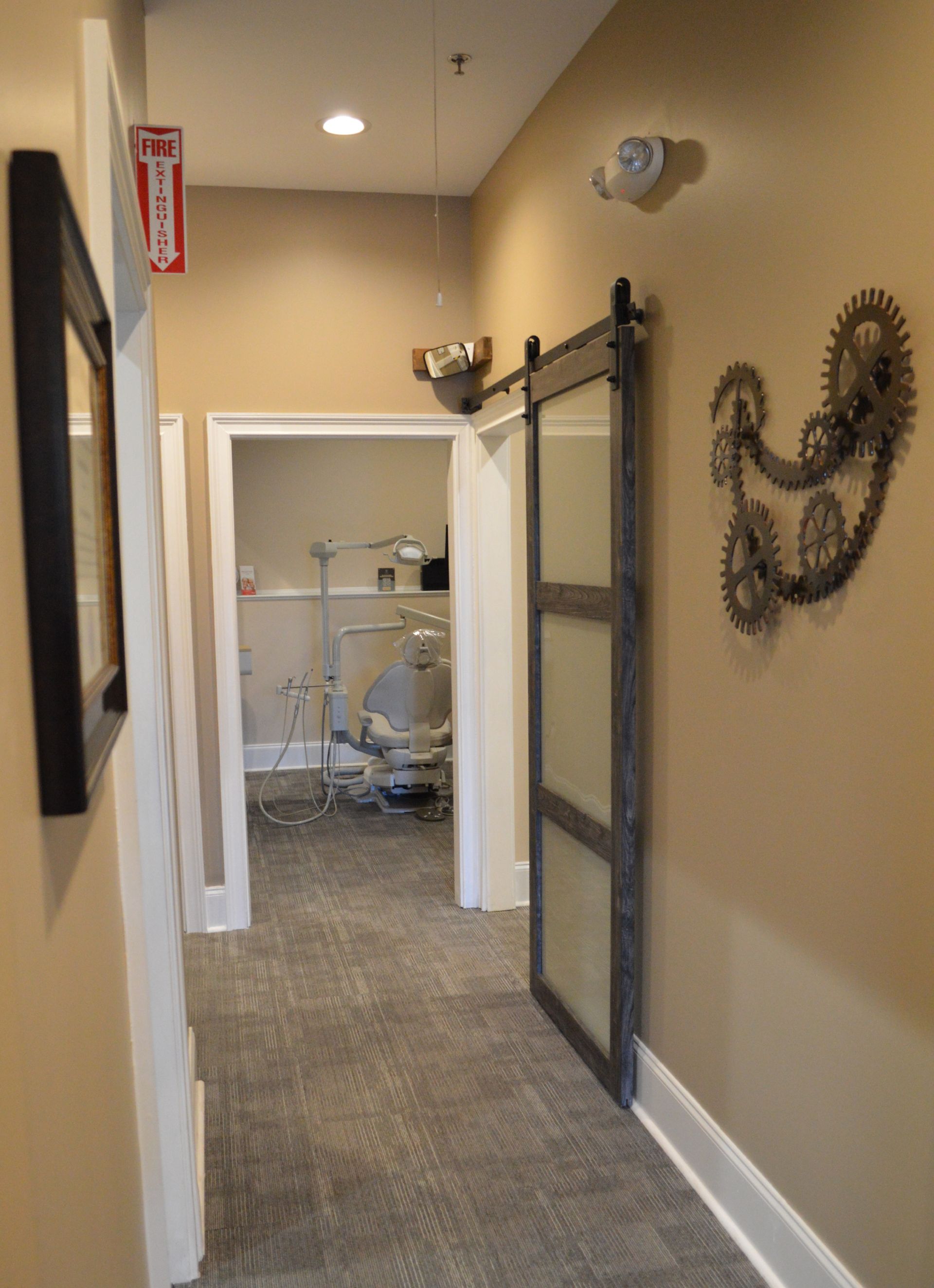 Hallway with dental office doors, gray carpet, sliding door, and wall decor.
