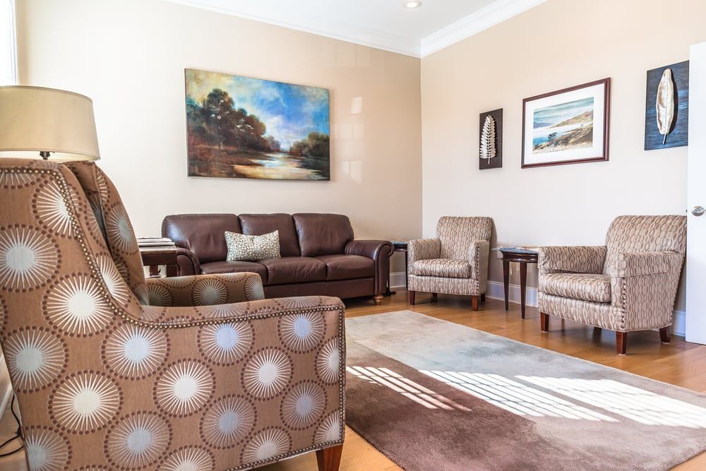 Living room with brown leather sofa, patterned armchairs, and landscape art.