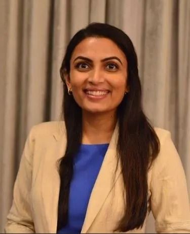Woman in beige blazer and blue top smiling, indoors.