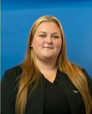 Woman with long blonde hair, wearing a black shirt, smiles against a blue backdrop.