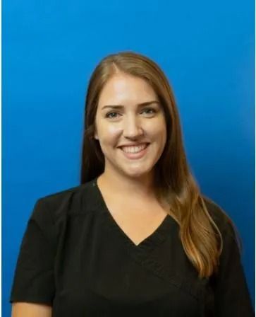 Woman with long brown hair smiling, wearing a black top, blue background.