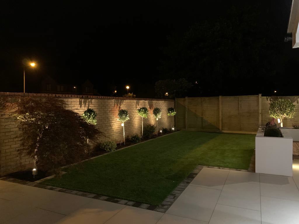 A backyard with a brick wall and a lush green lawn at night.