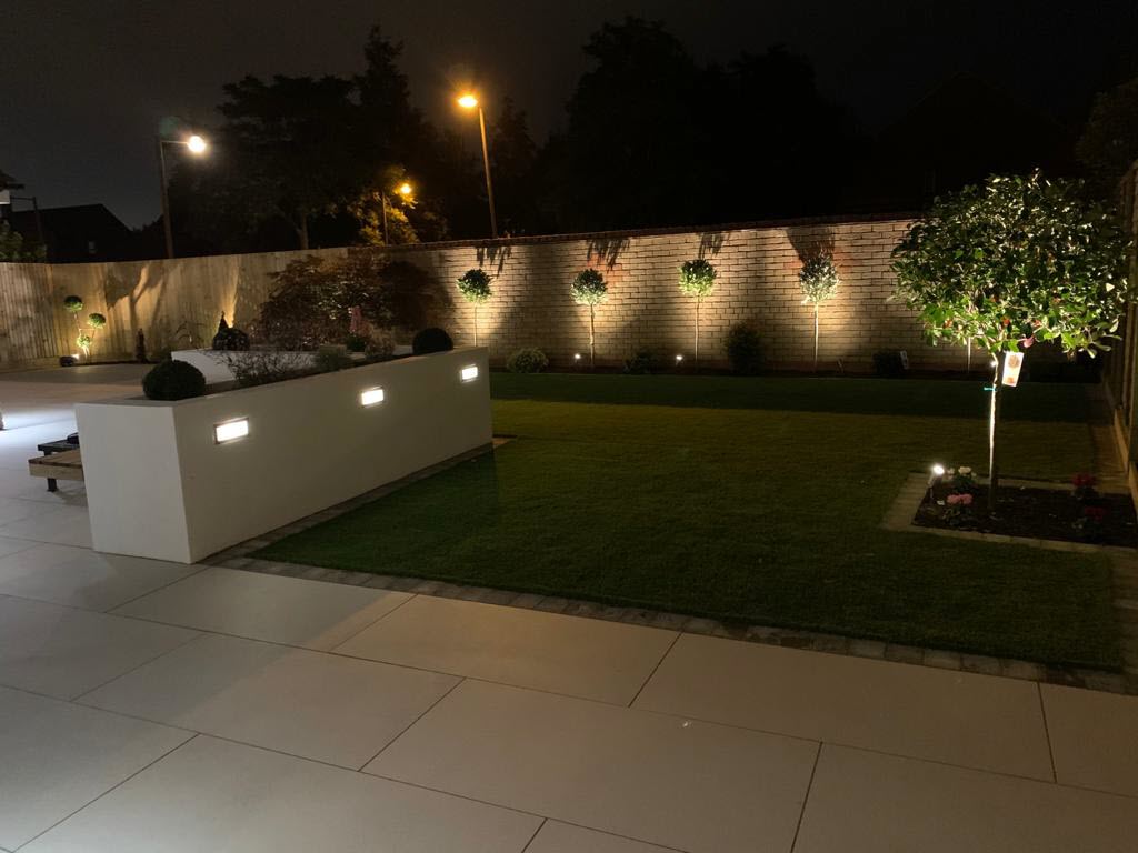 A backyard with a fence and a lawn is lit up at night.