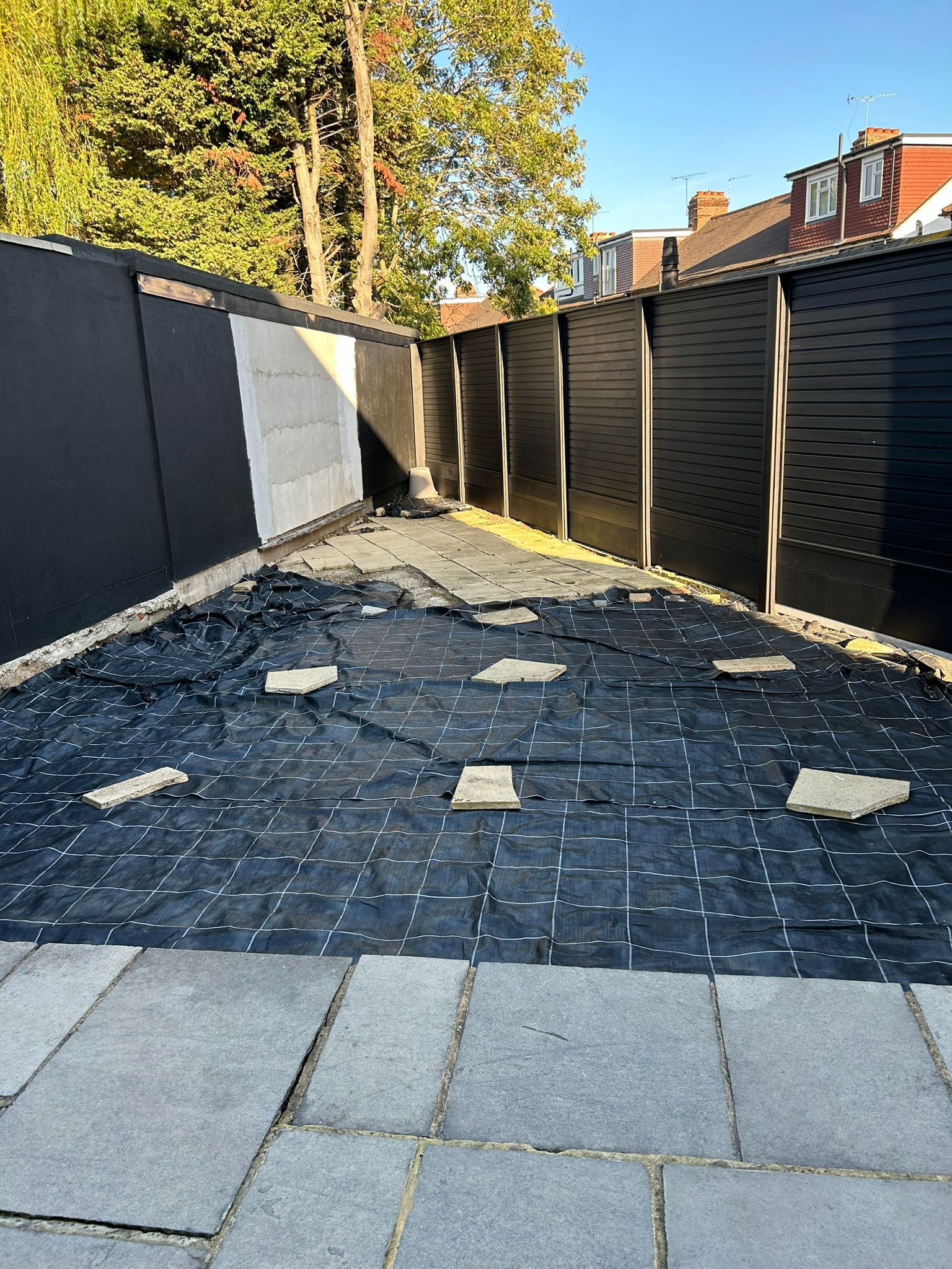 A backyard with a black fence and a black tarp on the ground.