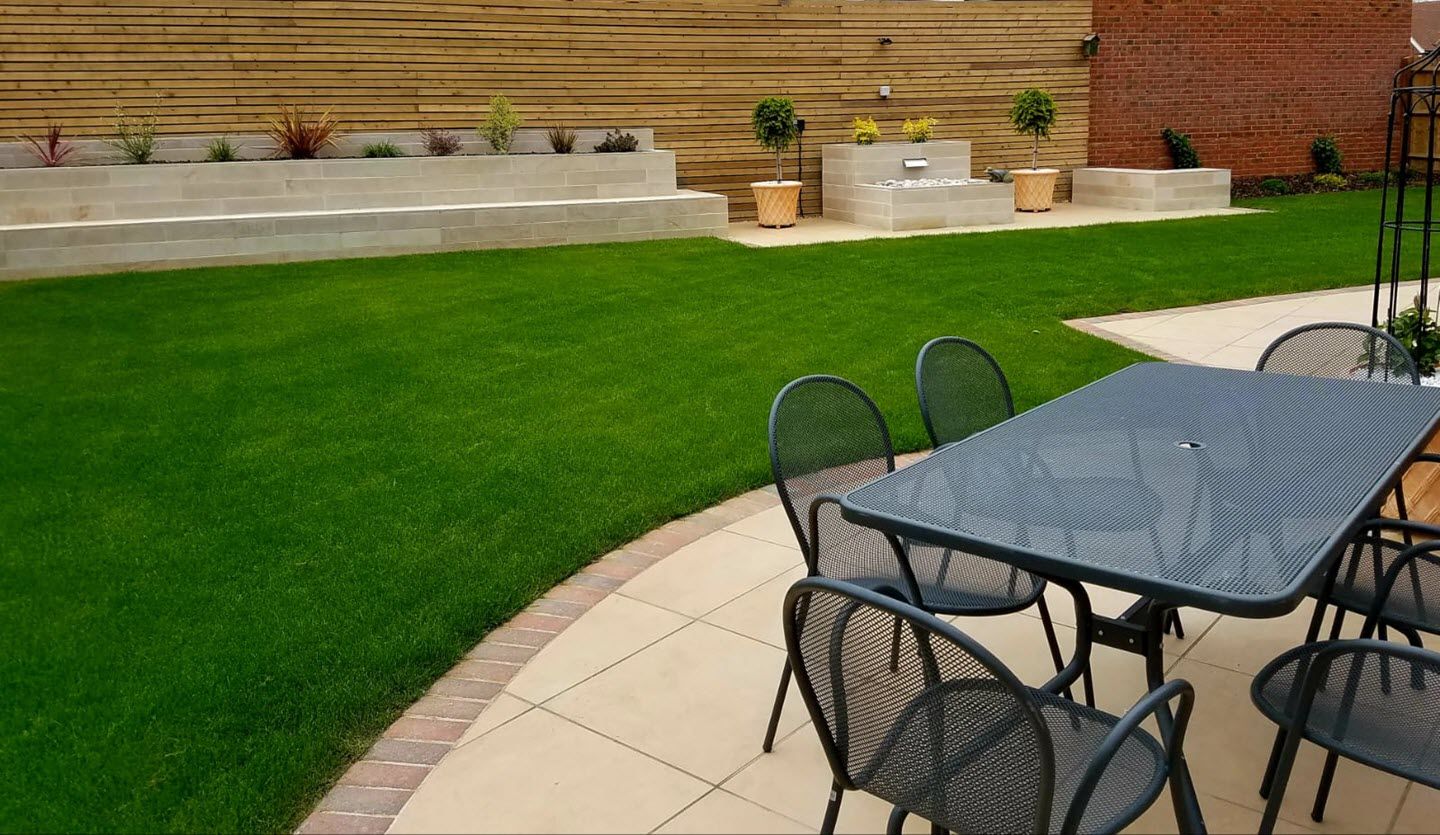 A patio with a table and chairs in front of a lush green lawn.