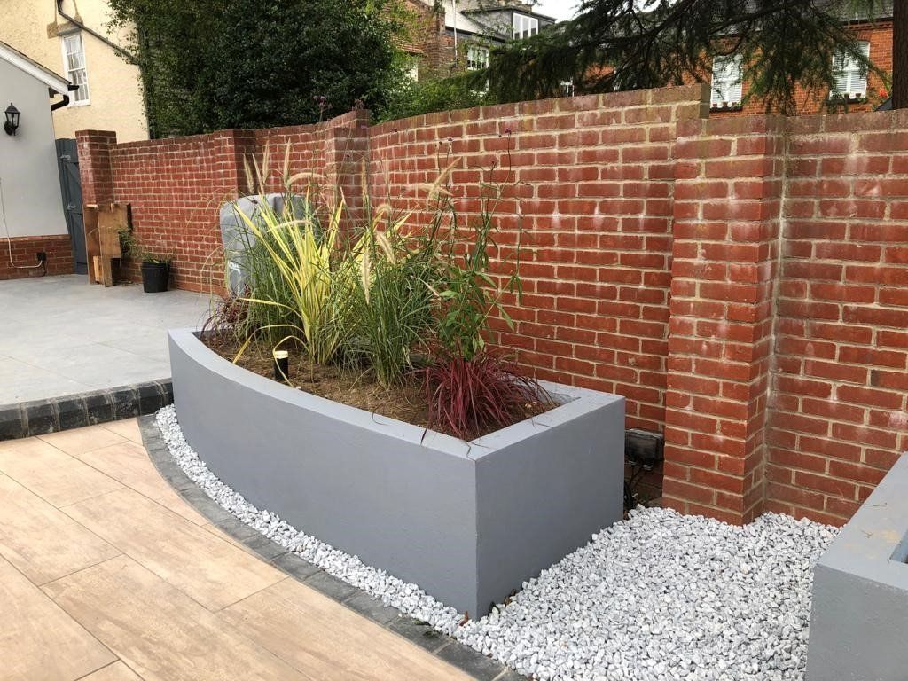 A curved planter filled with plants is sitting next to a brick wall.