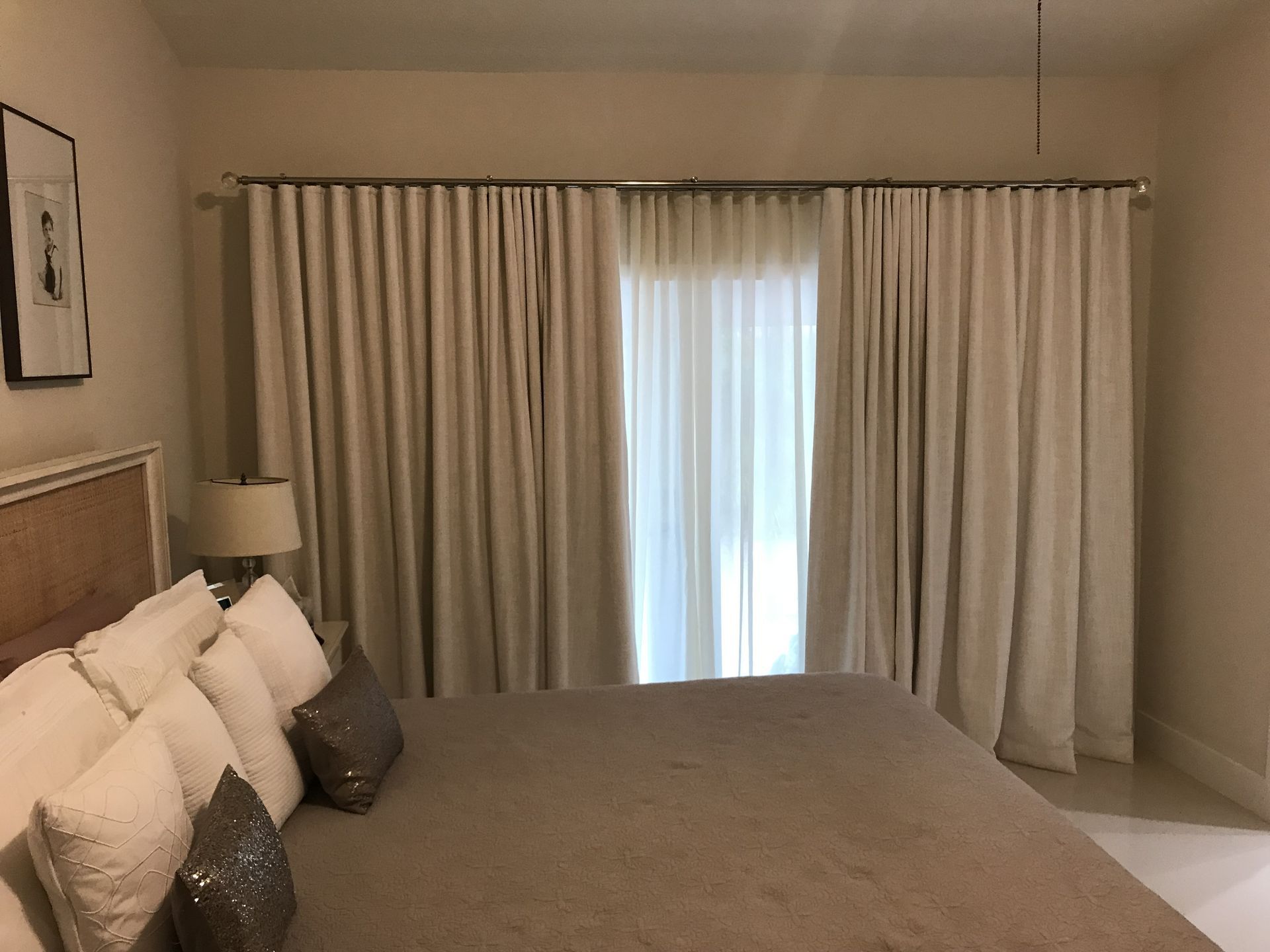 A bedroom with a bed , lamps , curtains and a large window.