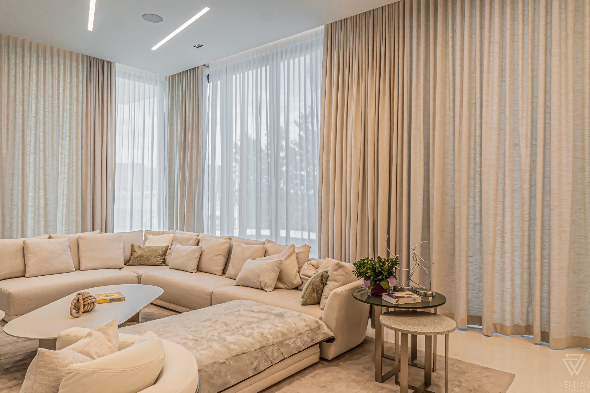 A living room with a large sectional couch , tables , and curtains.