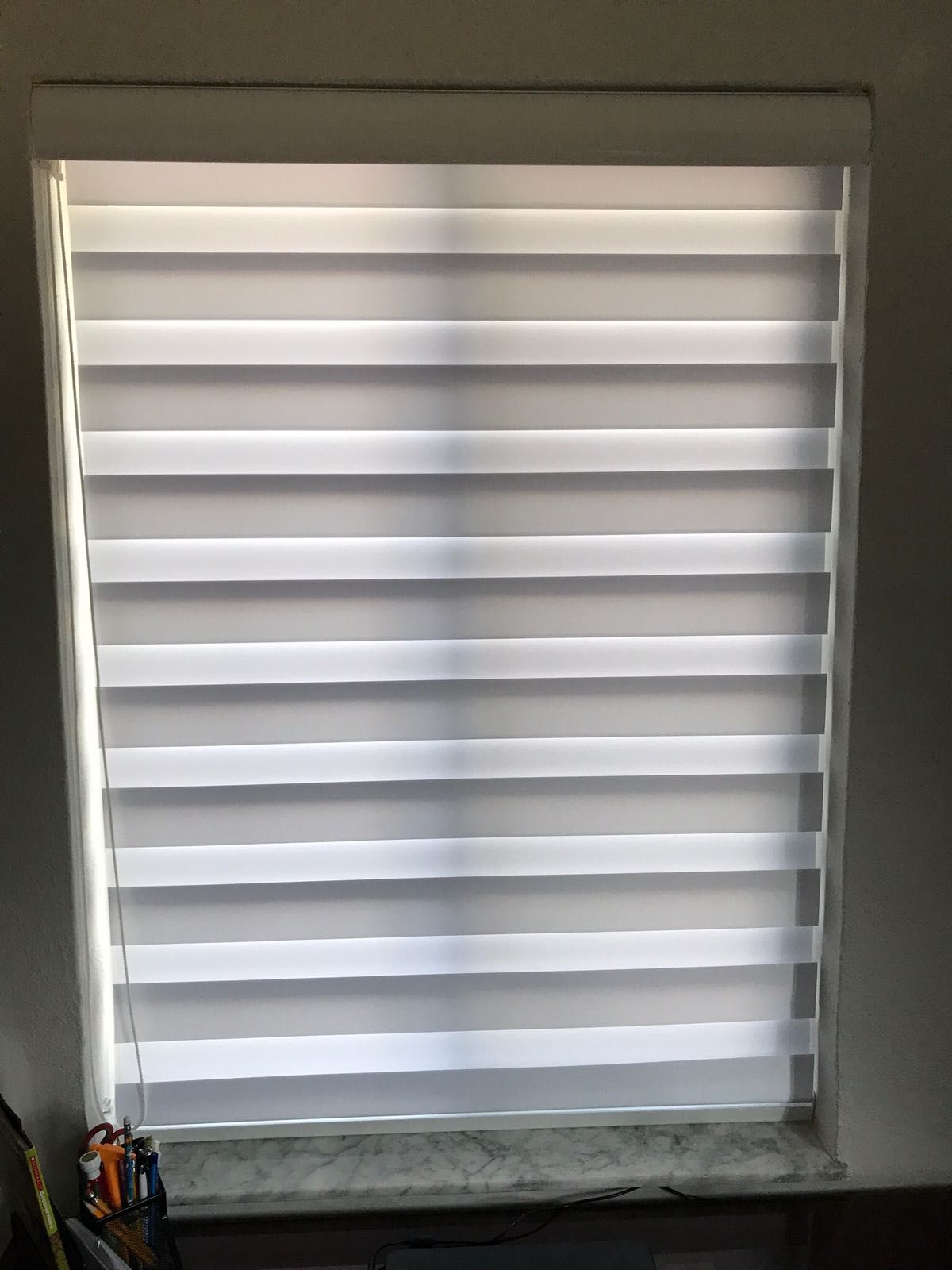 A white blind is sitting on a window sill in a room.