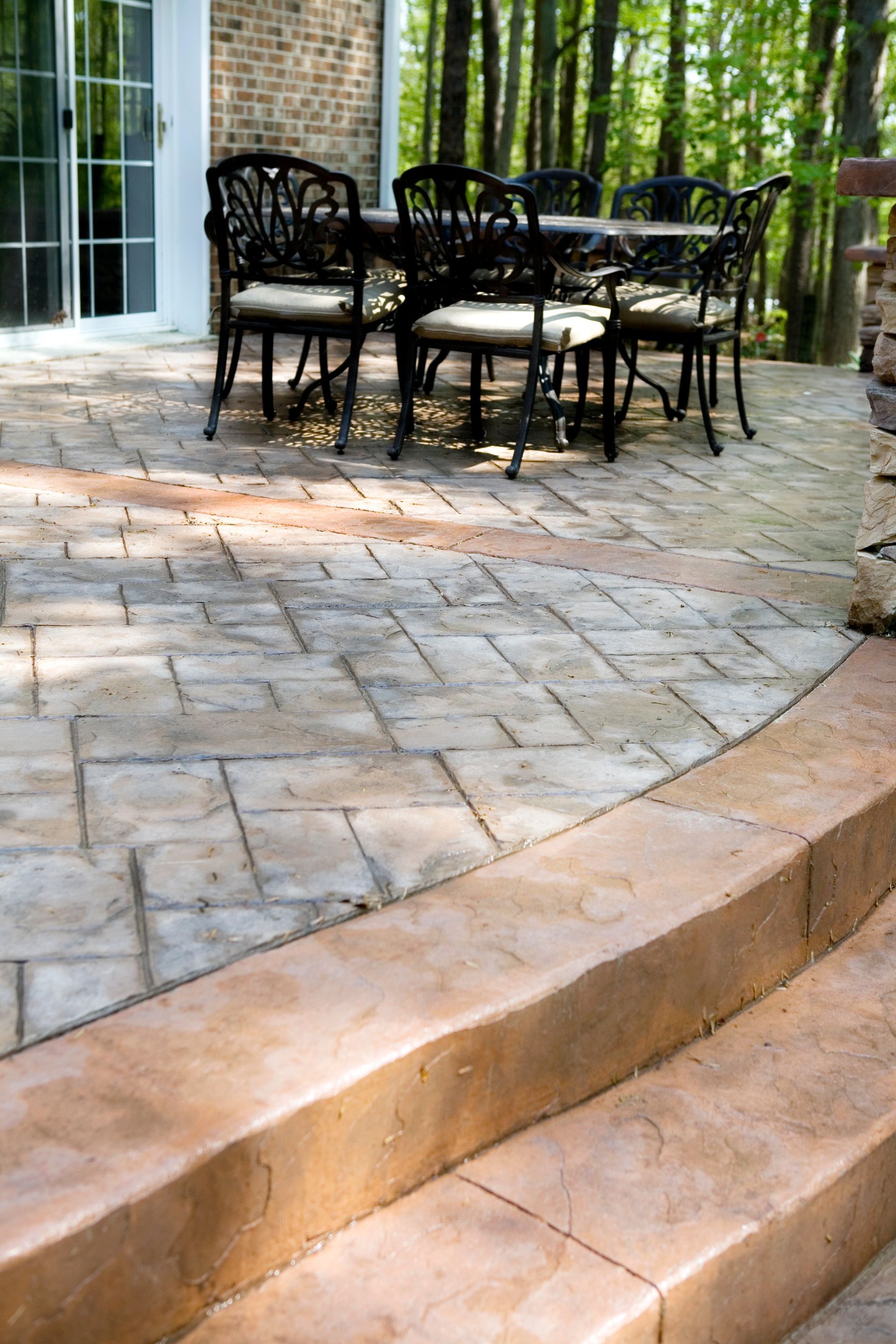 Stamped patio in a residential outdoor space with metal table, chairs, and trees in the background.