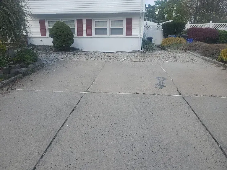 A concrete driveway leading to a white house with red shutters.