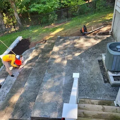 A man is laying concrete on the steps of a house.