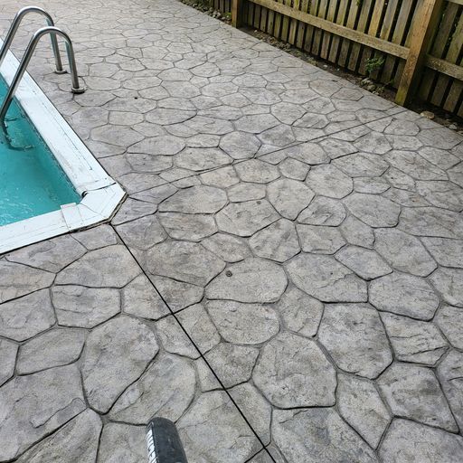 A concrete patio next to a swimming pool with stairs.