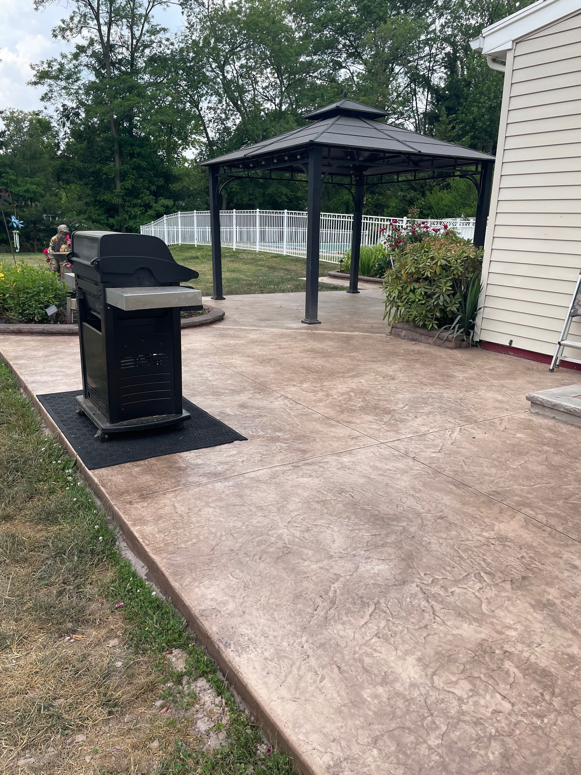 A grill is sitting on a concrete patio next to a gazebo.
