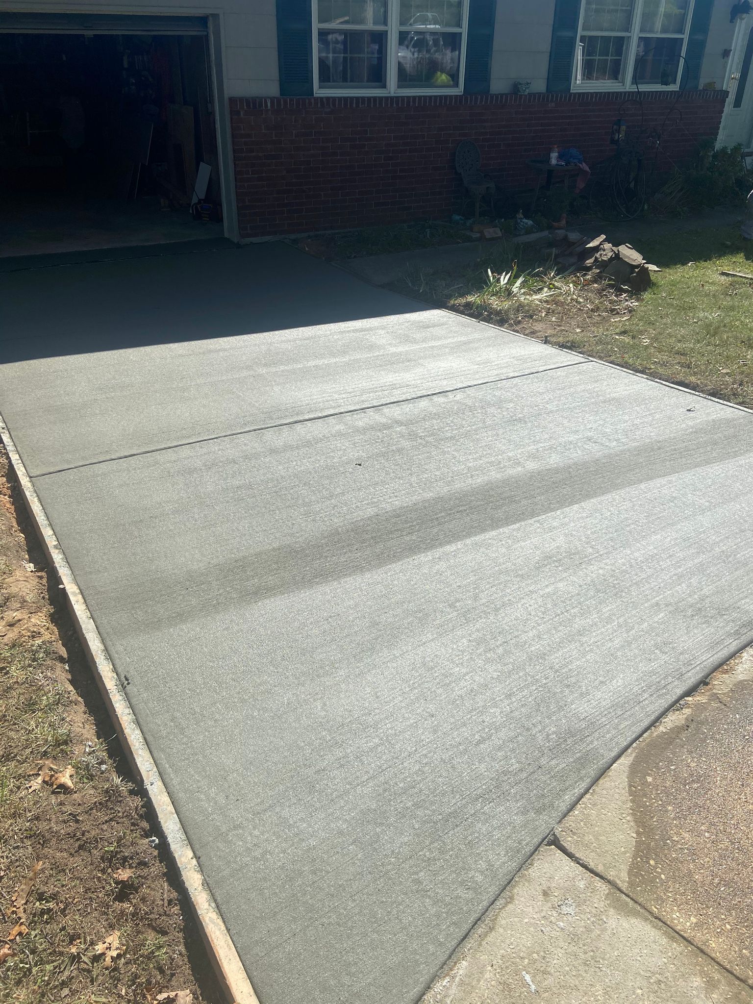 A concrete driveway is being built in front of a brick house.
