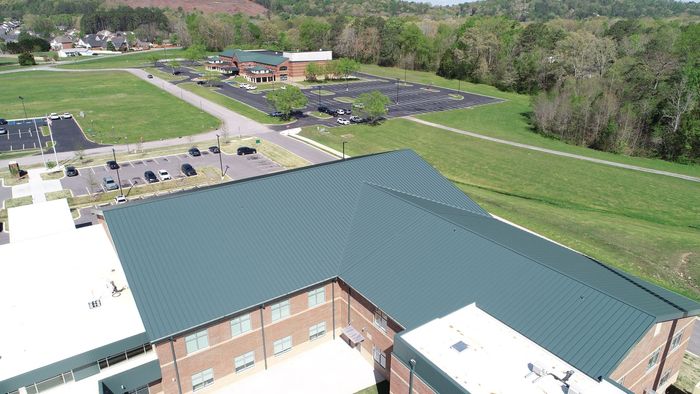 An aerial view of a large brick building with a green roof surrounded by trees.