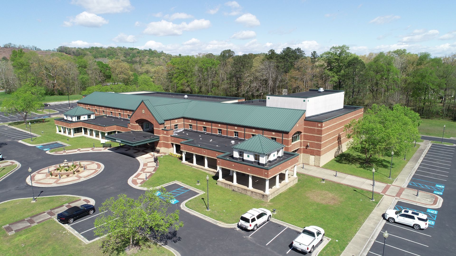 An aerial view of a large brick building with a green roof and cars parked in front of it.