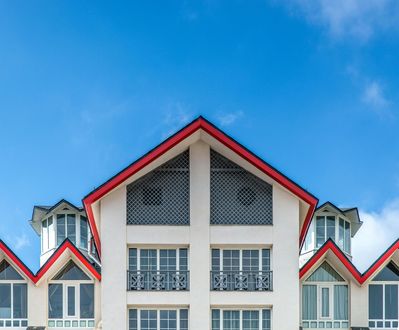 A symmetrical white building with a series of red-trimmed gables against a bright blue sky.