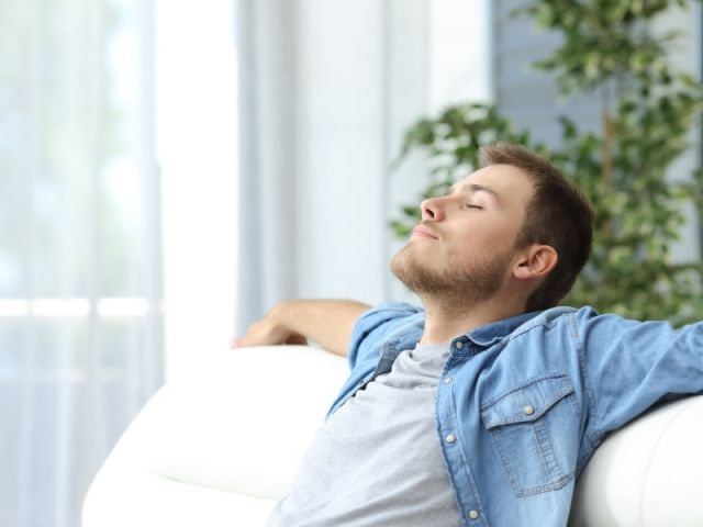 Un homme est assis sur un canapé, les yeux fermés.