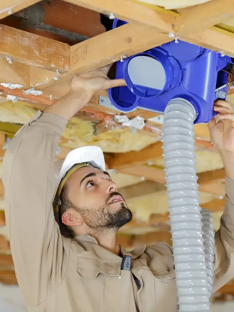 Un homme travaille sur un système de ventilation au plafond d'une maison.