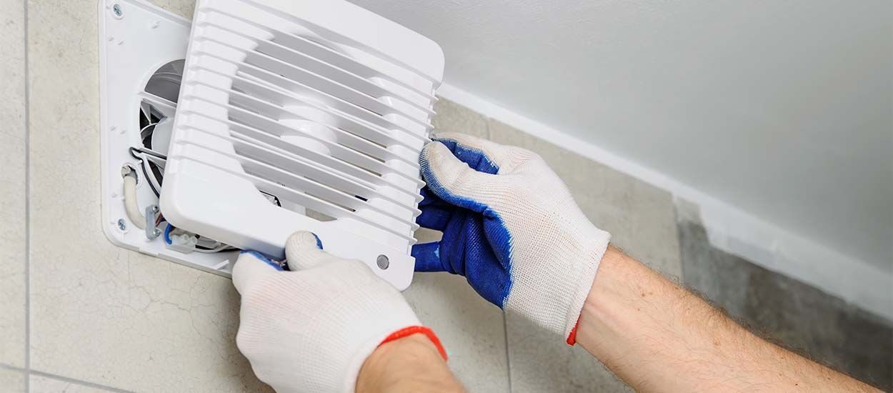Une personne installe un ventilateur sur un mur.