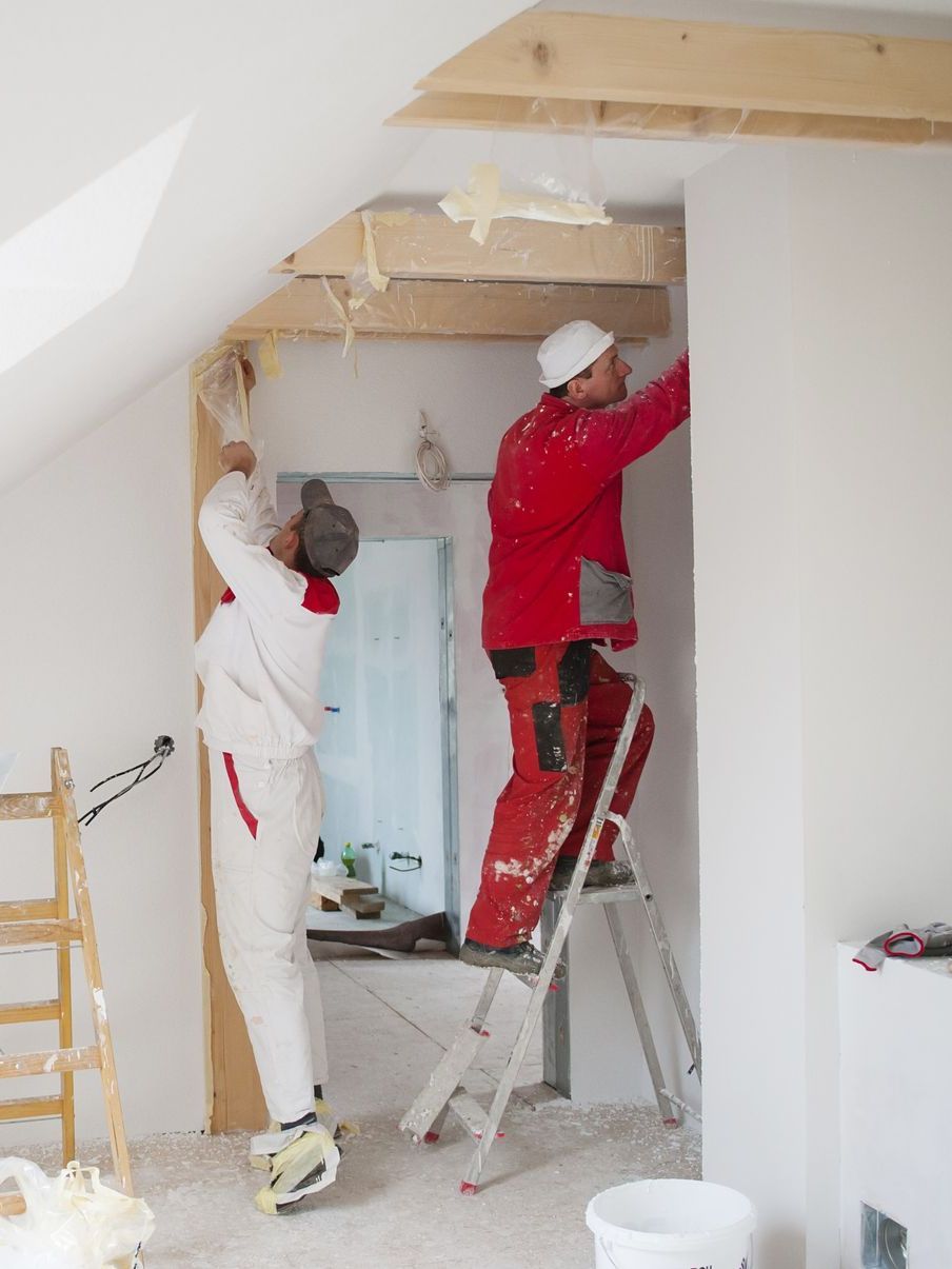 Deux hommes peignent un mur dans une pièce tandis que l'un d'eux se tient sur une échelle.