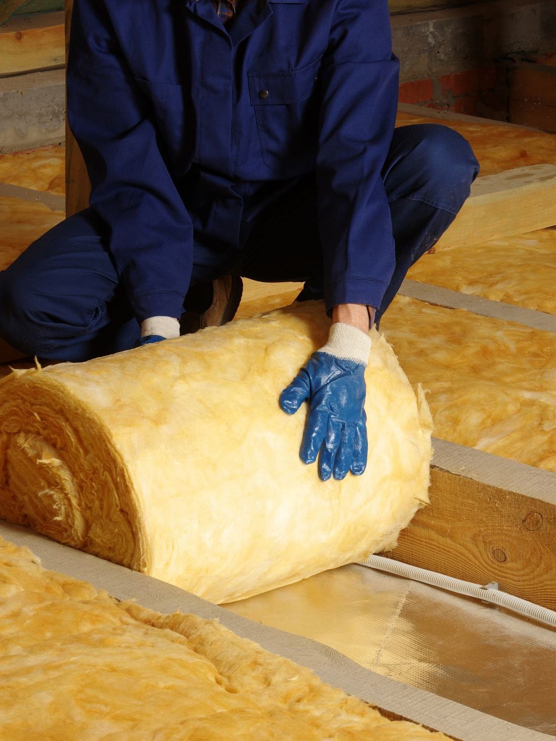Un homme portant des gants bleus est agenouillé à côté d'un rouleau d'isolant.