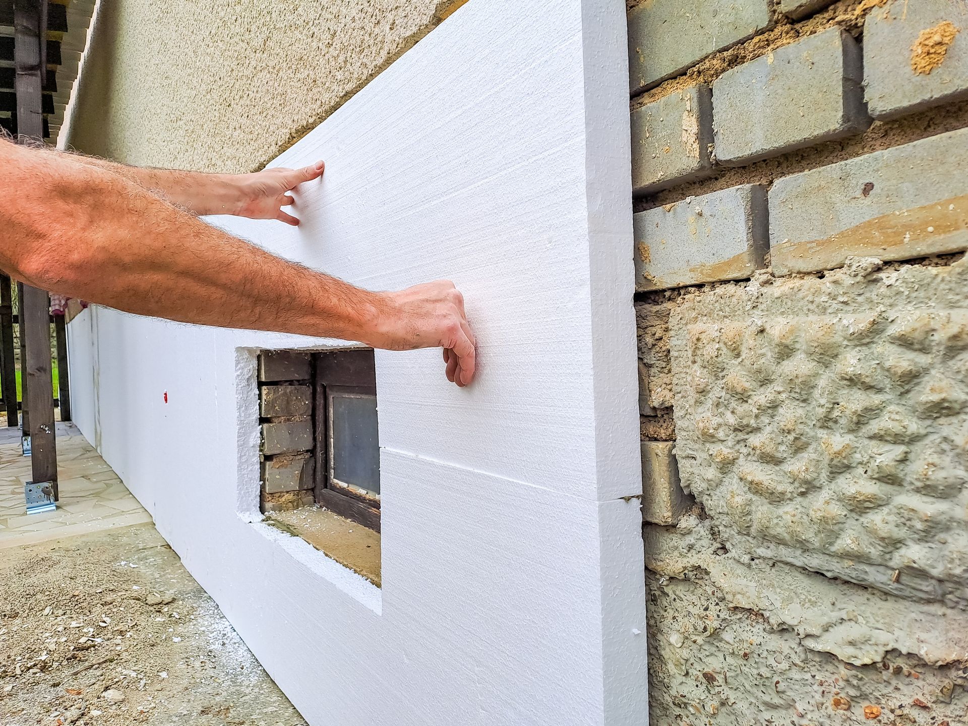 Un homme installe de l'isolant en polystyrène sur un mur de briques.
