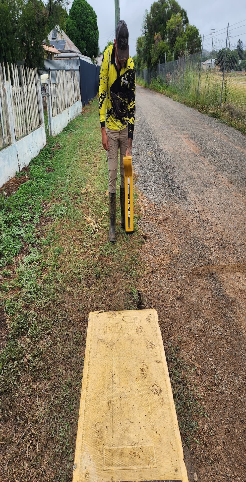 Person standing on dirt road, holding surveying equipment. A yellow rectangular concrete marker is in the foreground — ViperVac Solutions PTY LTD in Cannonvale, QLD