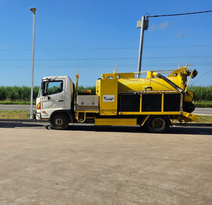 A Yellow Excavator Is Digging A Hole In The Ground — ViperVac Solutions PTY LTD in Cannonvale, QLD