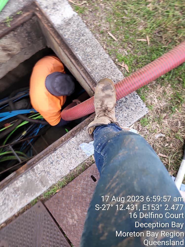 A Man Is Standing In A Manhole Cover With A Red Hose — ViperVac Solutions PTY LTD in Cannonvale, QLD