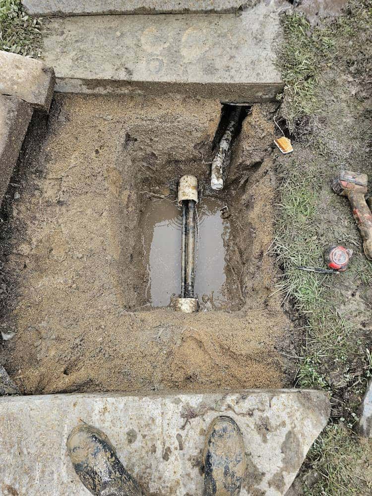 A Person Is Digging A Hole In The Ground With A Pipe In It — ViperVac Solutions PTY LTD in Cannonvale, QLD