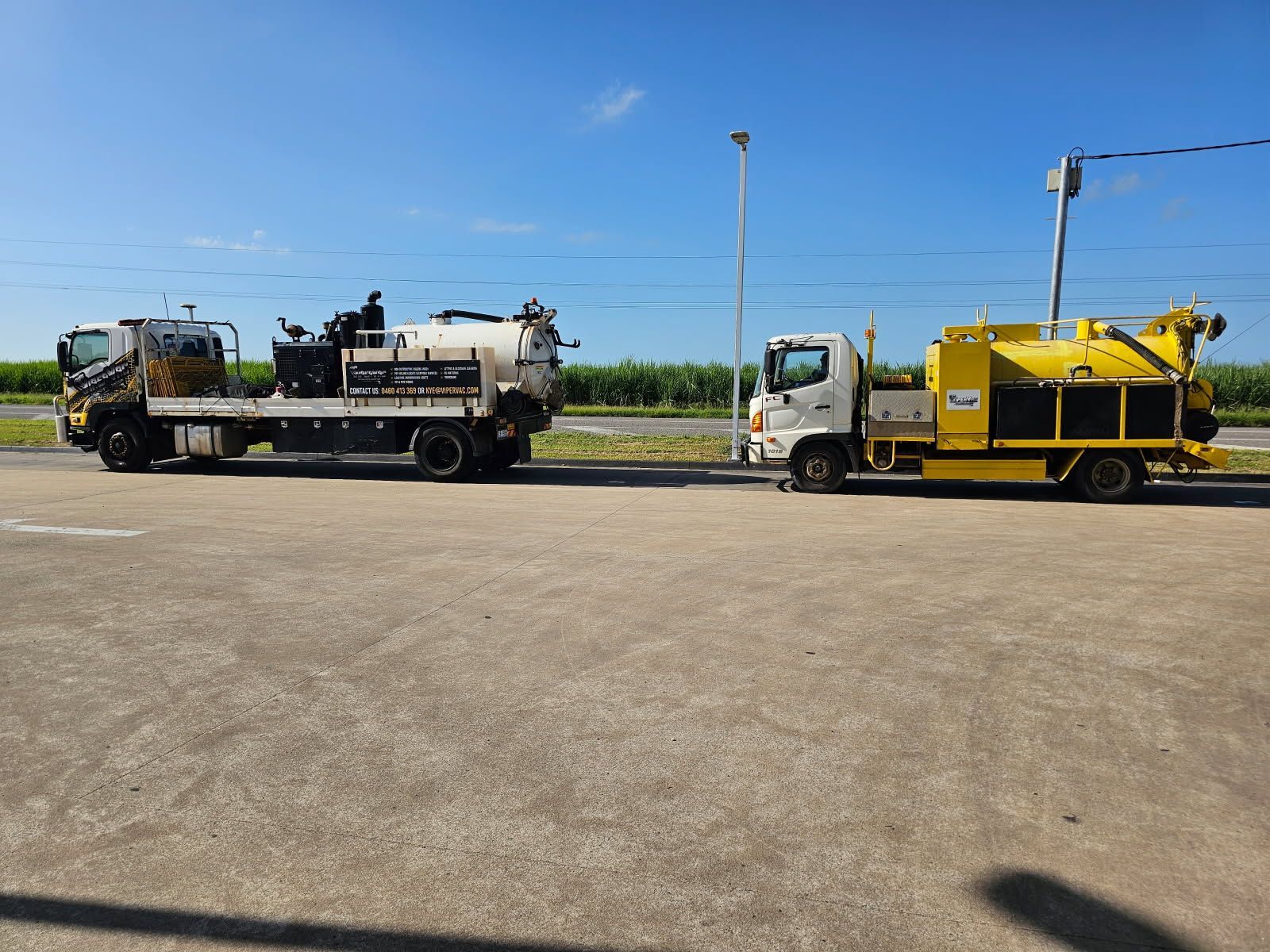 Two industrial trucks parked on asphalt under a blue sky, one white and one yellow — ViperVac Solutions PTY LTD in Cannonvale, QLD
