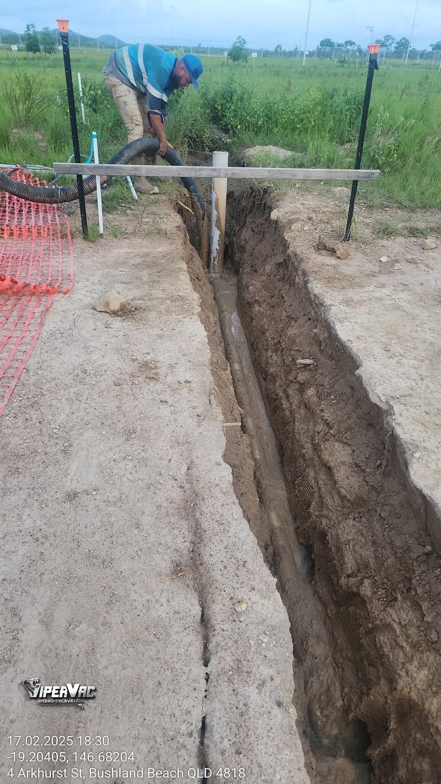 Man digging a trench in the dirt, wooden guide in place. A fence and open field in background — ViperVac Solutions PTY LTD in Cannonvale, QLD