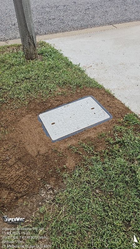 A rectangular utility cover in a grassy area next to a sidewalk and tree — ViperVac Solutions PTY LTD in Cannonvale, QLD