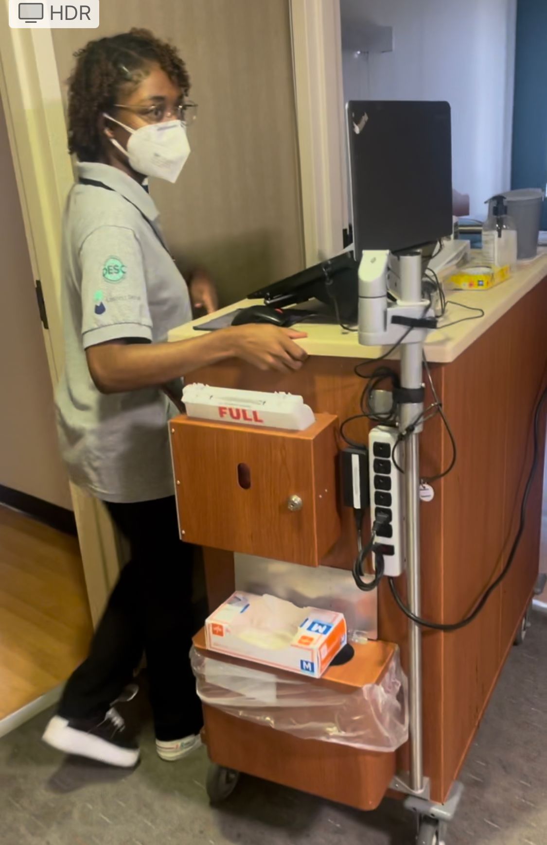 A woman wearing a mask is standing in front of a desk.