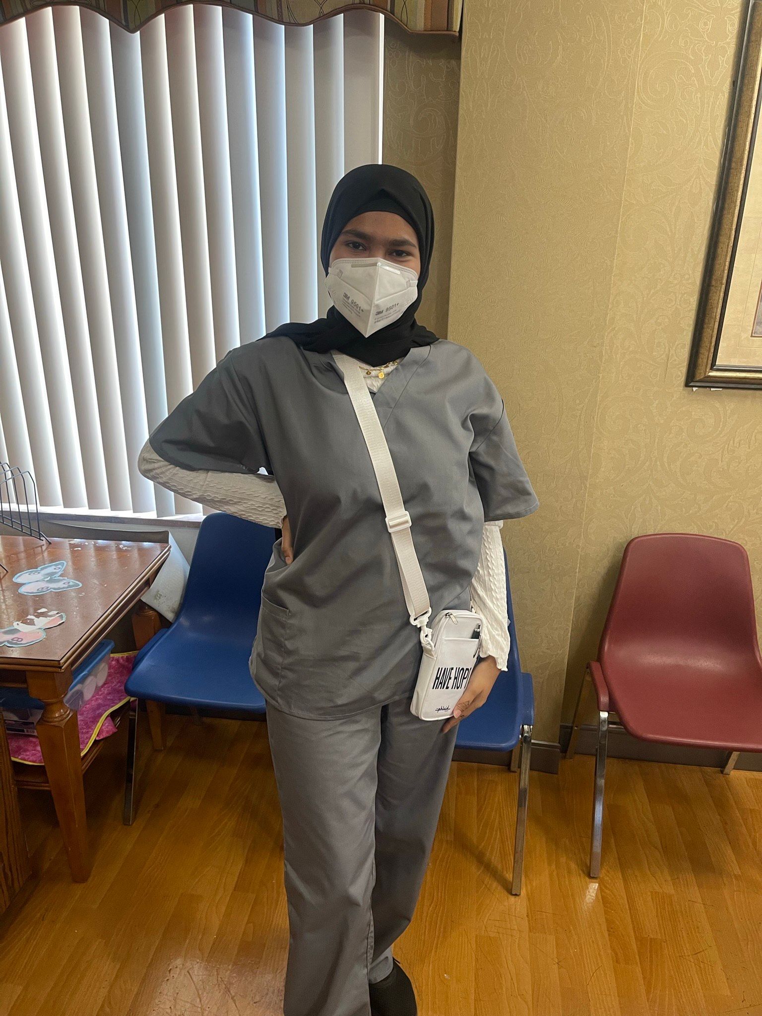 A woman wearing a mask and scrubs is standing in a waiting room.
