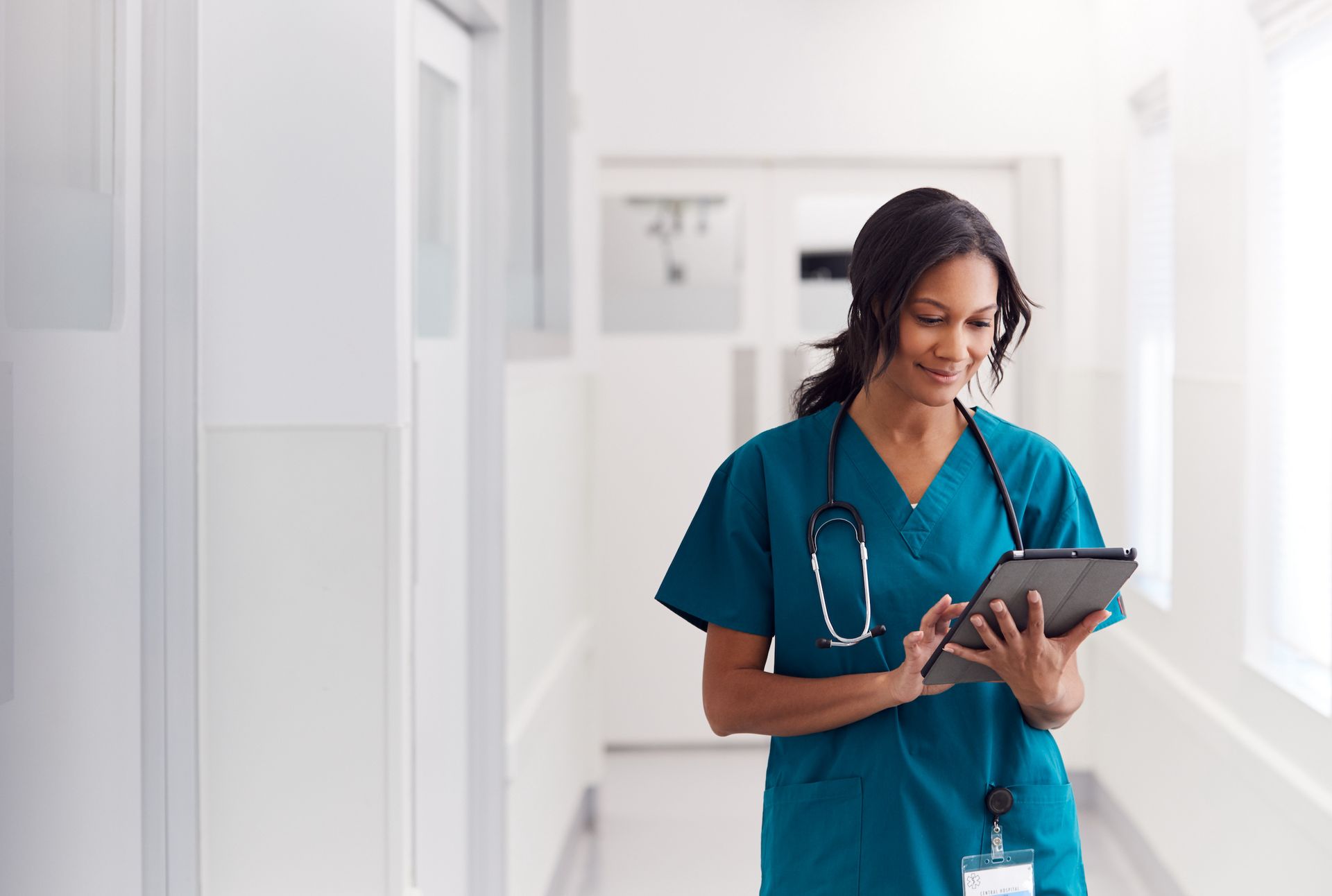 A nurse is using a tablet in a hospital hallway.